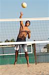 Young man jumping, hitting volleyball over net on beach