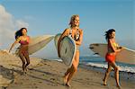 Three female surfers carrying surfboards, running on beach