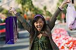 Teenage girl (16-17) raising shopping bags in street, (portrait)