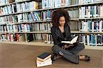 Young woman sitting on library floor, reading