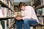 Male college student sitting, reading in library