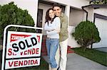 Couple standing in front of house with Sold sign, portrait