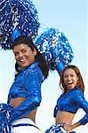 Cheerleaders with pom poms raised looking over shoulder