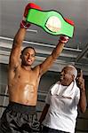 Boxer holding up champion belt with trainer