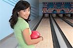 Young woman at bowling alley holding ball, portrait