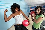 Young women at bowling alley holding balls and posing, portrait