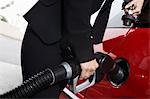 Businesswoman filling car at gas station, mid section