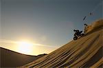 Men riding quad bikes in desert at sunset