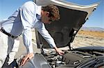 Man looking at engine of sports car by side of desert road