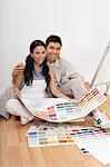 Couple looking at paint colour samples, sitting on floor, portrait