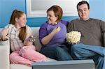 Overweight family watching television on sofa