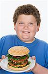 Overweight  boy holding plate with big cheeseburger
