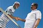 Deux hommes lui serrer la main au filet de tennis