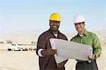 Bauarbeiter tragen Schutzhelme, Blick auf Plan vor Ort
