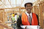 Smiling Surveyor in hard hat with building plans on Construction Site