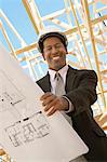 Smiling Surveyor in hard hat with building plans on Construction Site, low angle view