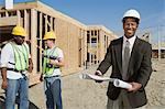 Two construction workers and surveyor holding blueprint