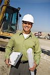 Surveyor holding blueprints on construction site, portrait