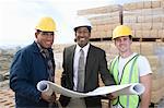 Three construction workers standing on construction site with blueprints