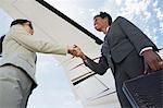 Businesswomen Shaking Hands below airplane wing, low angle view