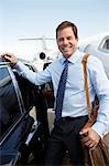 Smiling businessman standing beside car near private jet before Leaving on Business Trip