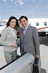 Portrait of mid-adult businesswoman and mid-adult businessman standing in front of private plane.