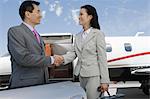 Mid-adult businesswoman and mid-adult businessman shaking hands in front of private plane.