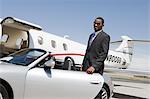 African-American businessman opening door of convertible on landing strip.