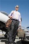 Senior businessman in front of car and airplane, low angle view.