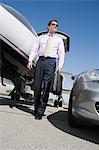 Mid-adult businessman in front of car and airplane, low angle view.