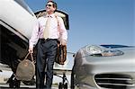 Mid-adult businessman in front of car and airplane.