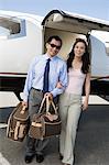 Portrait of mid-adult Asian business couple standing in front of private airplane.