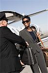 Mid-adult businesswoman giving suitcase to chauffeur in front of airplane