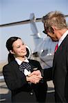 Mid-adult flight attendant and senior businessman shaking hands.