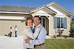 Portrait of mid-adult couple in front of new house, children (6-9) in background