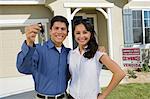 Young couple holding keys outside new home, portrait