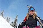 Teenage girl (16-17) holding skis, in front of snow covered hill