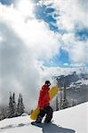 Teenage boy (16-19) holding snowboard, hiking up snow covered slope, full length