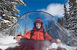 Woman driving snowmobile through snow, front view.