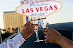 Two people toasting in front of  Welcome to Las Vegas sign