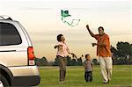 Couple and young son flying kite by car in park