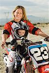 Mother and son (3-4) on motocross bike in desert, (portrait)