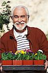 Elderly man holding tray with potted flowers