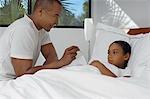 Male nurse taking temperature of girl (7-9) lying in bed