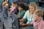 School children using computers with teacher in classroom