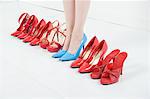 Line of red shoes with a woman standing in blue shoes