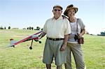 Senior couple standing on field, man holding model plane