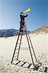 Businessman on Stepladder Using Megaphone in Desert