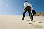Kaufmann zu Fuß bergauf mit Aktenkoffer in der Wüste
