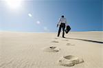 Homme d'affaires de marche en montée avec mallette dans le désert